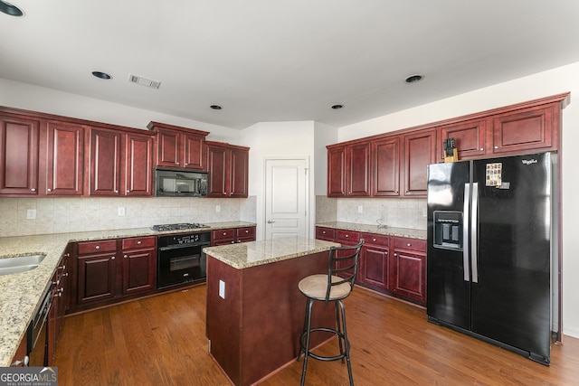 kitchen featuring tasteful backsplash, dark hardwood / wood-style flooring, a kitchen island, and black appliances