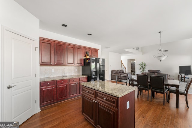 kitchen featuring backsplash, black fridge with ice dispenser, dark hardwood / wood-style floors, a kitchen island, and hanging light fixtures