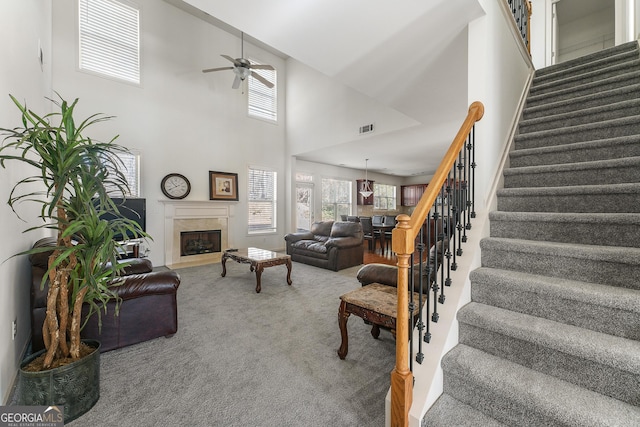 carpeted living room with a high end fireplace, a high ceiling, and ceiling fan