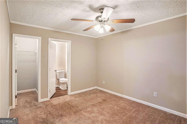 unfurnished bedroom with ensuite bath, ceiling fan, a textured ceiling, a walk in closet, and light carpet