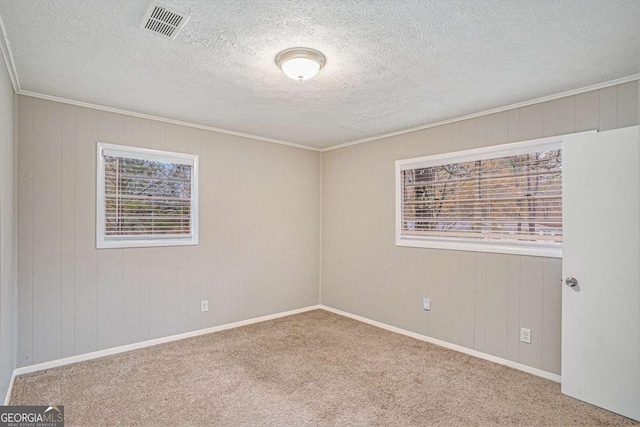 carpeted empty room with wood walls, a textured ceiling, and ornamental molding