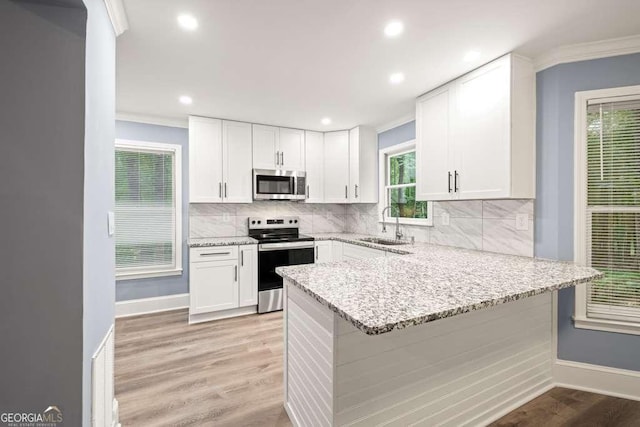 kitchen with white cabinets, crown molding, light stone countertops, appliances with stainless steel finishes, and kitchen peninsula