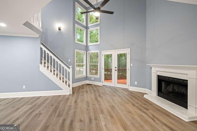 unfurnished living room featuring ceiling fan, light wood-type flooring, a high ceiling, and french doors