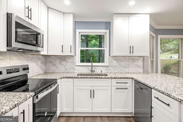 kitchen with appliances with stainless steel finishes, light stone counters, ornamental molding, sink, and white cabinets