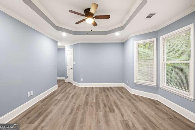 empty room with ceiling fan, ornamental molding, a tray ceiling, and light hardwood / wood-style flooring