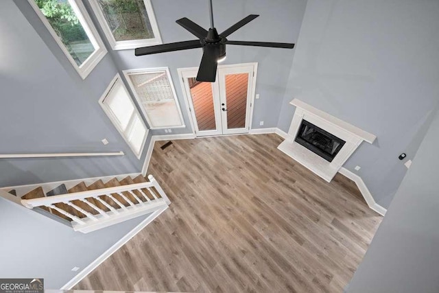 unfurnished living room with french doors, ceiling fan, a premium fireplace, a towering ceiling, and light hardwood / wood-style floors