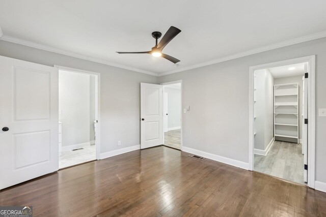 unfurnished bedroom with dark hardwood / wood-style flooring, a spacious closet, ceiling fan, and ornamental molding