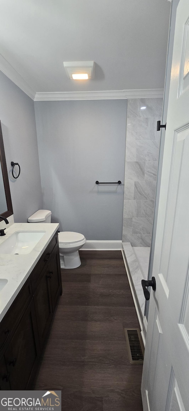 bathroom with crown molding, wood-type flooring, tiled shower, toilet, and vanity