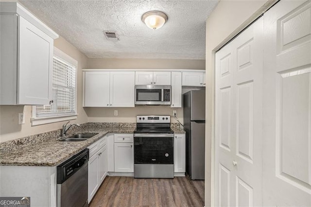 kitchen with dark wood-type flooring, sink, light stone countertops, appliances with stainless steel finishes, and white cabinetry