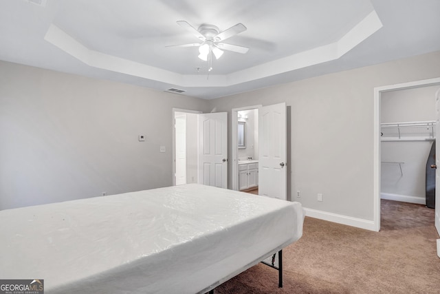 carpeted bedroom with a walk in closet, a closet, a raised ceiling, and ceiling fan