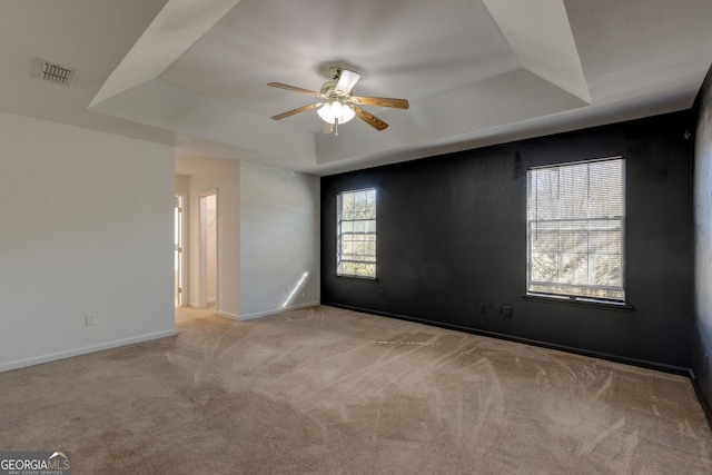 spare room featuring a tray ceiling, light carpet, and ceiling fan