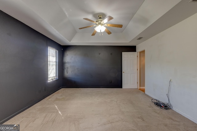 empty room featuring a tray ceiling, light carpet, and ceiling fan