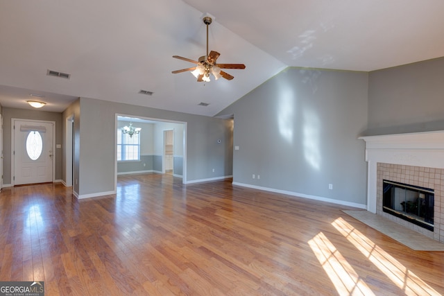 unfurnished living room with ceiling fan with notable chandelier, light hardwood / wood-style floors, lofted ceiling, and a tiled fireplace