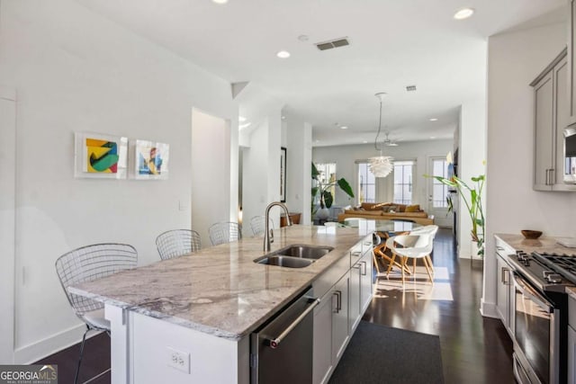 kitchen with light stone counters, a breakfast bar, stainless steel appliances, sink, and a center island with sink