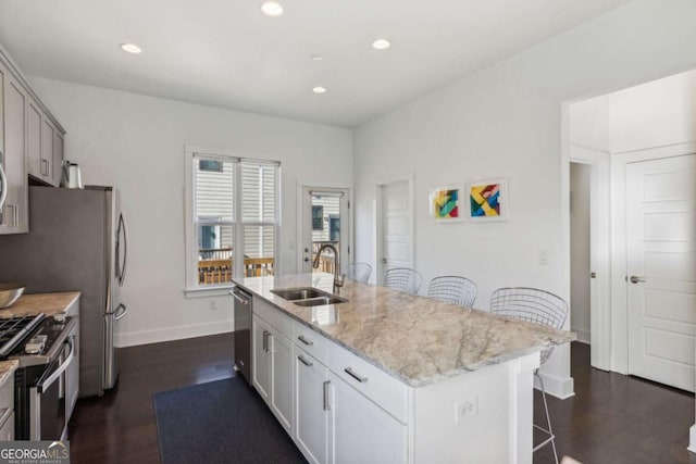 kitchen with a center island with sink, a kitchen breakfast bar, sink, light stone counters, and stainless steel appliances