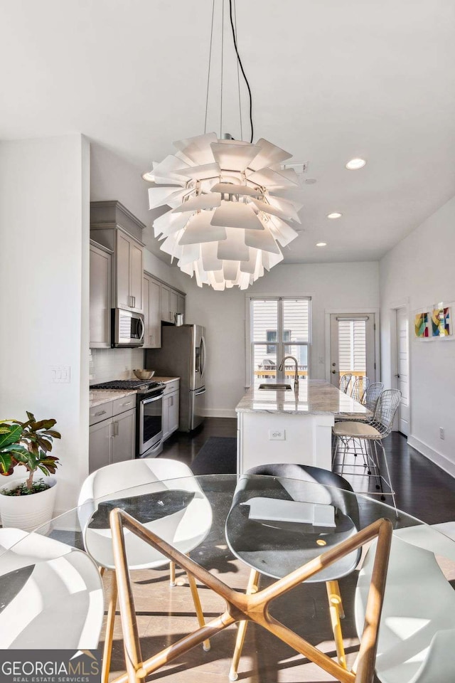 kitchen with light stone countertops, appliances with stainless steel finishes, dark hardwood / wood-style flooring, gray cabinetry, and a kitchen island with sink