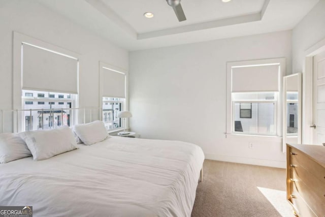 carpeted bedroom with a raised ceiling and ceiling fan