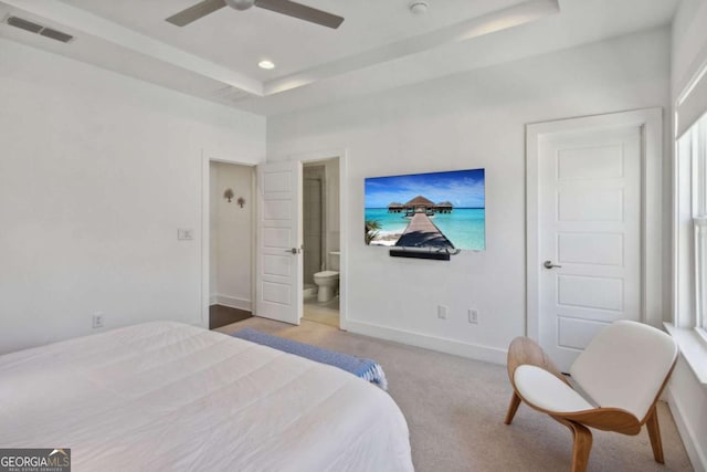 bedroom with a raised ceiling, ensuite bath, ceiling fan, and light carpet