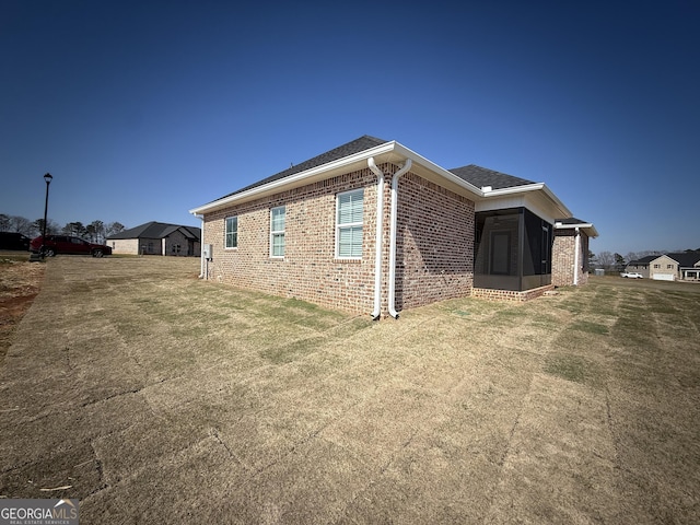 view of side of home with a shingled roof, a lawn, and brick siding