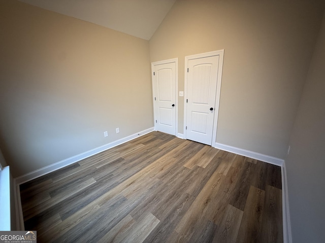 unfurnished bedroom featuring baseboards, vaulted ceiling, and dark wood-style flooring