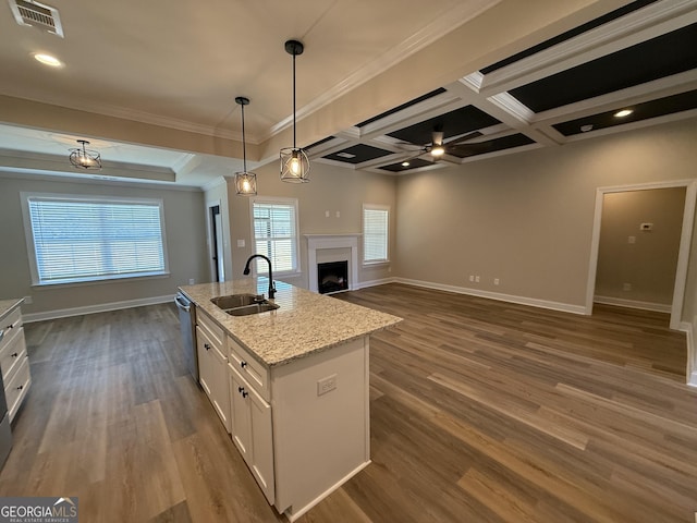 kitchen featuring decorative light fixtures, a fireplace, white cabinetry, a sink, and an island with sink