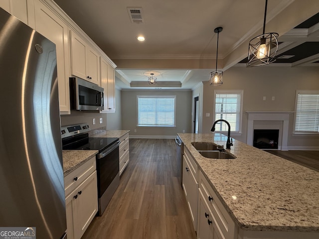 kitchen with decorative light fixtures, a center island with sink, stainless steel appliances, open floor plan, and white cabinetry