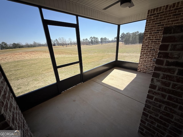 unfurnished sunroom featuring a ceiling fan and a rural view