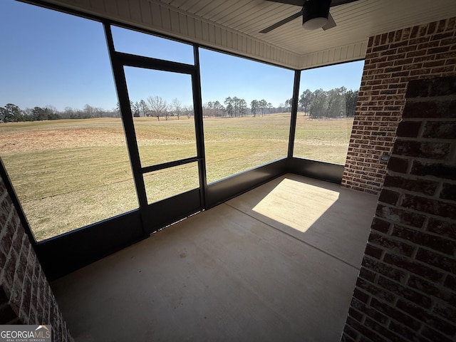 unfurnished sunroom featuring ceiling fan and a rural view