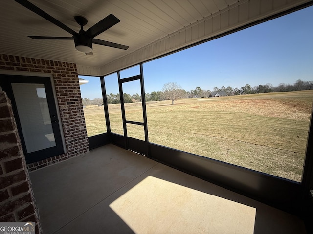 unfurnished sunroom featuring a rural view and a ceiling fan