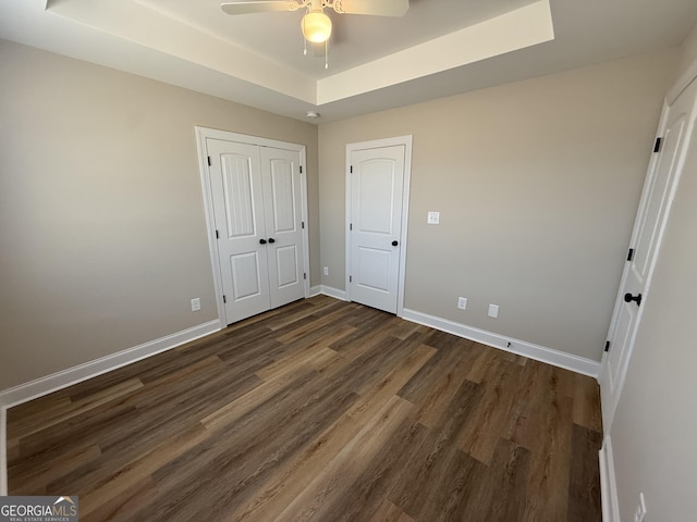 unfurnished bedroom with baseboards, a raised ceiling, a ceiling fan, dark wood-style floors, and a closet