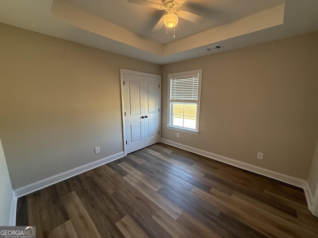 unfurnished bedroom featuring visible vents, baseboards, dark wood-type flooring, a tray ceiling, and a closet