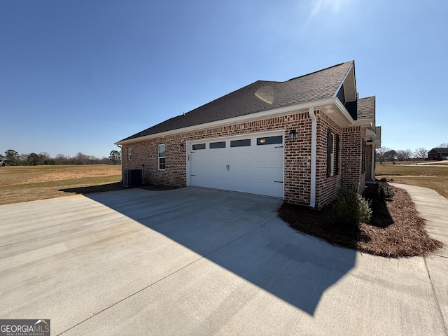 view of side of property with brick siding, driveway, an attached garage, and roof with shingles