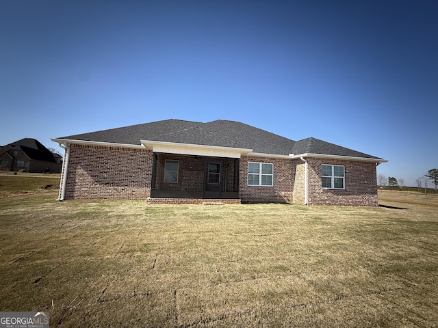 rear view of house featuring brick siding, a lawn, and a shingled roof