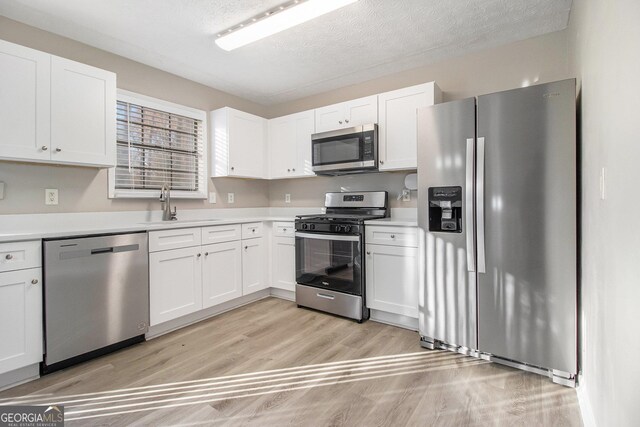 kitchen with a textured ceiling, stainless steel appliances, sink, white cabinets, and light hardwood / wood-style floors