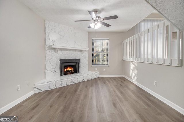 unfurnished living room with hardwood / wood-style floors, a textured ceiling, a stone fireplace, and ceiling fan