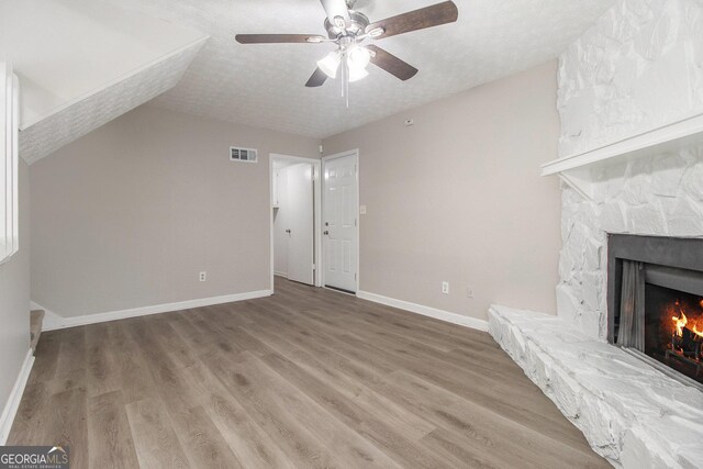 unfurnished living room with a stone fireplace, wood-type flooring, and a textured ceiling