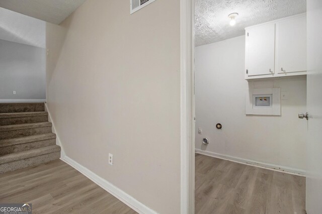 clothes washing area with washer hookup, cabinets, light wood-type flooring, and a textured ceiling