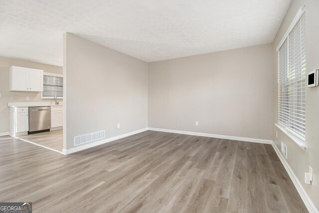 unfurnished living room featuring a textured ceiling, light hardwood / wood-style floors, a healthy amount of sunlight, and sink