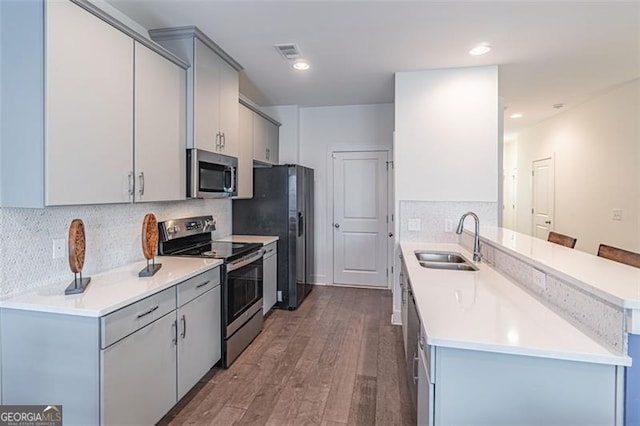 kitchen with gray cabinetry, sink, a kitchen bar, wood-type flooring, and stainless steel appliances