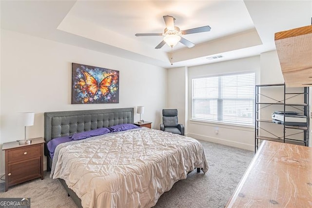 carpeted bedroom with ceiling fan and a tray ceiling