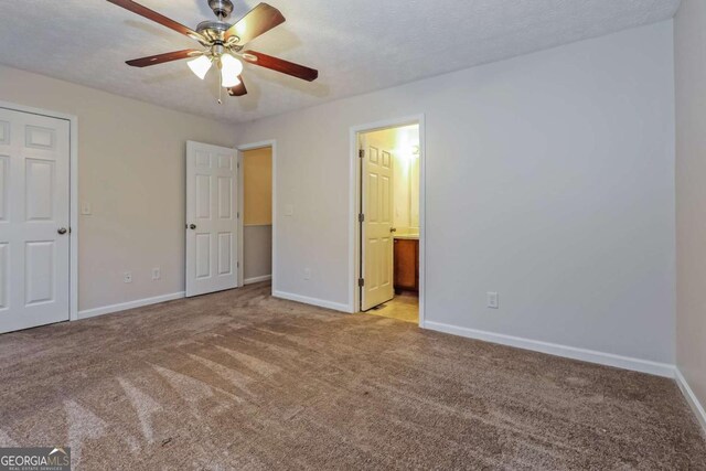 unfurnished bedroom featuring a textured ceiling, light colored carpet, ensuite bath, and ceiling fan