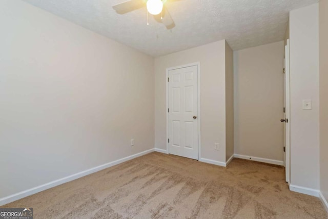 unfurnished bedroom featuring ceiling fan, light colored carpet, and a textured ceiling