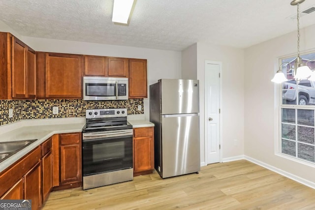 kitchen featuring pendant lighting, backsplash, light wood-type flooring, appliances with stainless steel finishes, and a notable chandelier