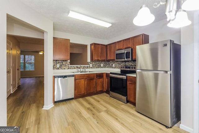 kitchen featuring sink, hanging light fixtures, stainless steel appliances, tasteful backsplash, and light hardwood / wood-style floors