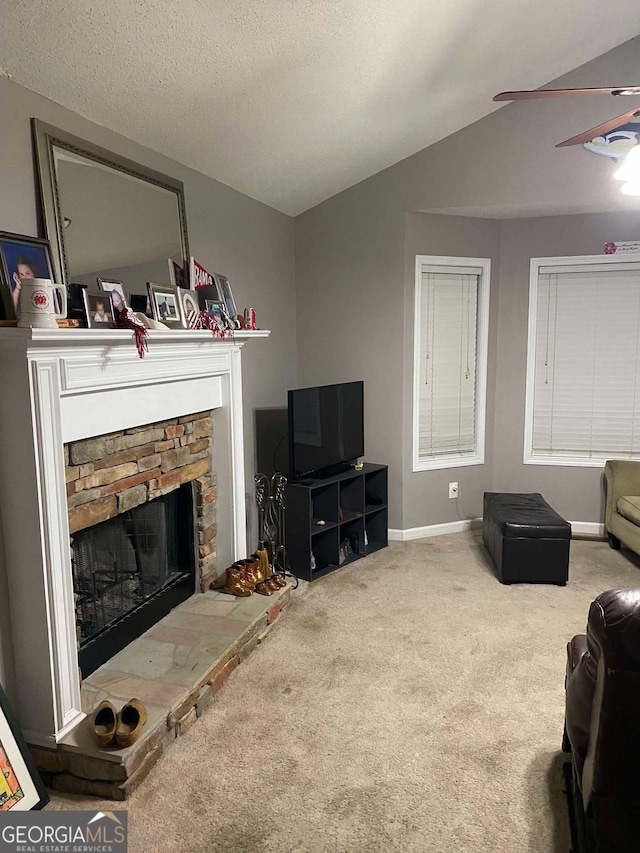 living room featuring lofted ceiling, ceiling fan, carpet, a textured ceiling, and a stone fireplace