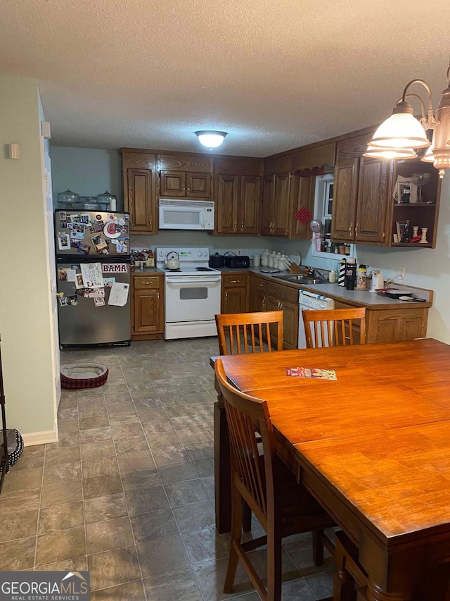 kitchen featuring sink, a textured ceiling, white appliances, and decorative light fixtures