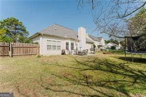 rear view of property with a trampoline and a lawn