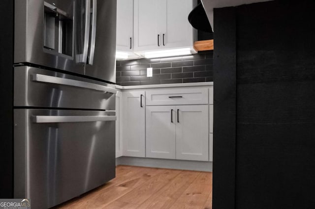 kitchen featuring black refrigerator, backsplash, white cabinets, stainless steel fridge with ice dispenser, and light hardwood / wood-style floors