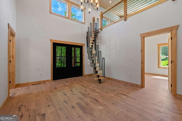 entryway featuring french doors, a towering ceiling, a chandelier, and light wood-type flooring