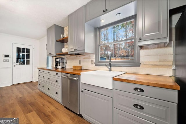 kitchen featuring light hardwood / wood-style flooring, sink, butcher block countertops, stainless steel dishwasher, and decorative backsplash